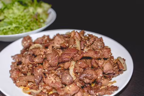 减肥能不能吃鸡心?热量怎么样?哪些优缺点? Fried cumin lamb with onion on white plate, on black background, chinese food.
